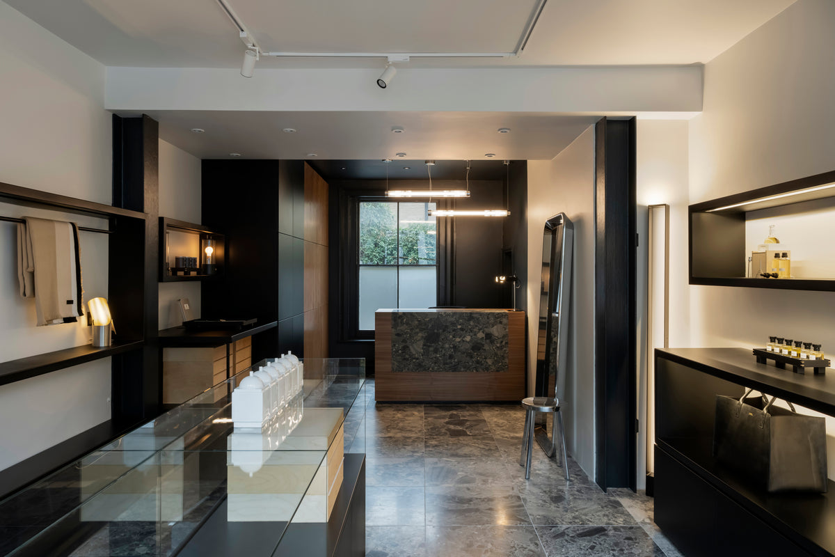 The interior view of Tuckson shop on 75 Westbourne Park Rd W2 5QH, with Tuckson signature marble floors and retail counter, Tuckson eau de parfum on the black metal units. Stainless steel mirror and chairs. 