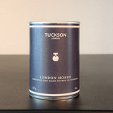Tuckson London honey can on a dark surface with a light background