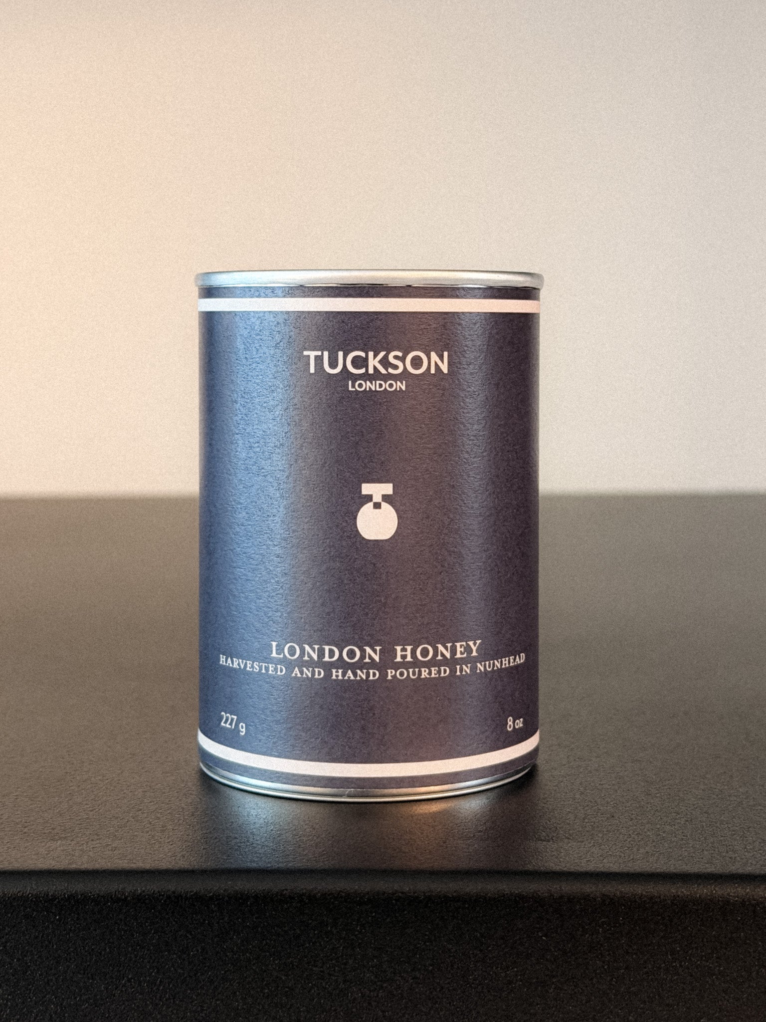 Tuckson London honey can on a dark surface with a light background